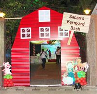 A grand entrance to a barnyard theme 1st birthday replicating a life size barn entrance with a doorway for guests to walk through. A farmer with his barn animals at the entrance to welcome to guests. 